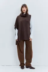 Poncho asimétrico de tejido de punto en color marrón, con cuello alto tipo polera y diseño sin mangas con aberturas laterales.