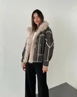 Gamulán de cuero sintético en color gris oscuro, con interior y bordes de piel sintética en tono crema. Presenta un diseño con costuras visibles y paneles geométricos, cierre frontal con botones a presión y bolsillos laterales.