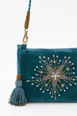 Cartera tipo bandolera de terciopelo color verde petróleo, con bordado central de estrellas en pedrería y mostacillas. Incluye una borla decorativa lateral y correa trenzada con detalles metálicos.