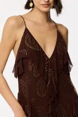 Vestido largo marrón de viscosa con estampado paisley formado por apliques termoadhesivos dorados. Presenta escote en V con tirantes finos, volantes en cascada y una abertura lateral profunda en la falda.