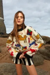 Sweater de lana tejido a mano color crudo, con cuello redondo y puños negros. Presenta bordados de figuras abstractas en colores rojo, azul, amarillo, verde y naranja.