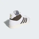 Championes Adidas Jabbar Hi de corte alto, con exterior de cuero blanco, detalles de gamuza marrón en las icónicas tres tiras y en el cuello, y suela de caucho en tono crema.