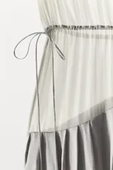 Vestido largo de tirantes con escote redondo, confeccionado en mezcla de viscosa. Presenta un diseño combinado con la parte superior en tejido ligero semitransparente y la parte inferior con volumen y drapeado asimétrico.