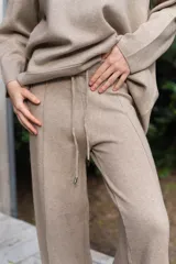 Conjunto de dos piezas color tostado, compuesto por un buzo de cuello redondo con mangas largas y hombros caídos, y un pantalón de corte recto con cintura elástica y cordón ajustable.