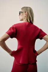 Top peplum confeccionado en hilatura de algodón de color bordó, con escote en V pronunciado, mangas cortas abullonadas y bajo con vuelo.