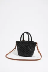 Bolso tipo cesta de estructura rígida y diseño trenzado en color negro. Cuenta con dos asas superiores cortas y una correa larga ajustable en color marrón. Incluye un dije circular decorativo con grabado en tono madera.