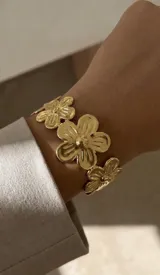 Brazalete rígido de acero dorado compuesto por diseño de flores unidas.