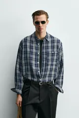 Camisa de corte relajado confeccionada en tejido fluido con mezcla de viscosa y acetato. Presenta un diseño a cuadros, cuello solapa, manga larga con puños abotonados, bolsillo plastrón en el pecho y cierre frontal con botones.