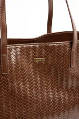 Bolso tipo shopper color marrón de cuero sintético con diseño trenzado. Cuenta con doble asa de hombro y placa metálica con el logo de la marca en el frente.