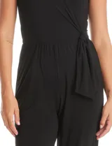 Enterito de seda fría color negro, con escote en V cruzado, mangas cortas decoradas con apliques de brillo y perlas, cintura elástica con lazo lateral ajustable y pierna de corte recto.