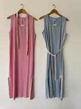 Vestido largo sin mangas color rosado, con escote redondo, bolsillos laterales y detalles de pasamanería en zigzag beige en el cinturón y los tajos laterales.