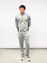 Conjunto deportivo Umbro compuesto por campera con cierre frontal y pantalón a juego. La campera presenta cuello alto, mangas largas con bloques de color azul en los hombros y logo de la marca bordado en el pecho. El pantalón es de corte recto y diseño liso, confeccionado en tejido sintético con acabado satinado.