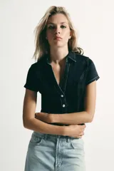 Camisa de denim entallada con cuello solapa, escote en pico y manga corta. Presenta costuras marcadas y cierre frontal con botones.