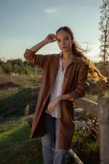 Gabardina marrón de cuero ovino italiano, con cuello camisero, cierre frontal con botones, mangas largas y corte recto.