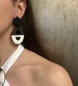 Aros colgantes con forma geométrica, con base superior en forma de rombo negro, y base inferior con forma de medialuna dividida en dos colores: marrón jaspeado y blanco.