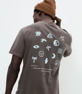 Remera de corte comfort color gris oscuro, con cuello redondo y mangas cortas. Presenta un pequeño estampado frontal con íconos étnicos y lettering en color blanco.
