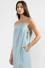 Vestido largo hasta el tobillo color celeste, de tejido arrugado liviano, con escote recto y breteles finos. Presenta lazos en los costados, forro hasta arriba de las rodillas y caída posterior más larga.