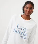 Pijama largo de dos piezas en tejido fleece. Incluye un buzo blanco de manga larga con bordado "Lazy Sunday Mood" en el frente y un pantalón largo con estampado de cuadros beige, negro y azul.