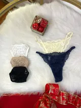 Pack de tres tangas de encaje con diseño floral, breteles regulables y laterales finos. El conjunto incluye una tanga rosa claro, una tanga color tostado con bordes grises y una tanga roja.