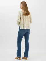 Blusa de algodón con estampado floral de flores silvestres sobre fondo claro. Presenta cuello redondo con detalle de puntilla, abotonadura frontal, canesú con frunces y mangas largas con puños elásticos decorados con puntilla.