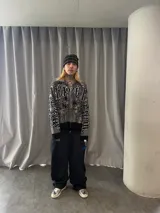 Buzo con cierre frontal completo, confeccionado en tejido de punto grueso de algodón. Presenta un diseño estampado integral con motivos gráficos y tipografía estilo gótico en tonos gris y negro, capucha integrada, puños y ruedo acanalados en color negro sólido.