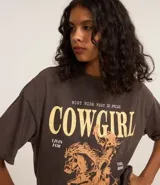 Remera de algodón con efecto lavado vintage, cuello redondo y mangas cortas. Presenta una estampa frontal contrastante con diseño de una mujer montando a caballo y lettering con la palabra Cowgirl.