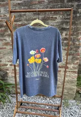 Remera azul con efecto lavado, de corte holgado y manga corta. Estampa en la espalda con flores de colores y la frase "Más flores, menos drama".