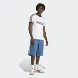 Short de jean estilo bermuda de corte holgado, color azul medio. Presenta las icónicas tres rayas laterales de Adidas en tono más claro y cierre de botón frontal. Incluye bolsillos delanteros y traseros.