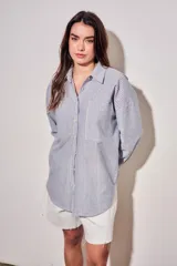 Camisa de corte oversize con diseño de rayas verticales en tonos azul y blanco. Presenta cuello clásico, cierre frontal con botones y mangas largas con puños abotonados.