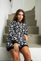 Vestido corto de punto con diseño oversize, cuello redondo y mangas largas. Presenta un estampado floral en contraste de color negro y blanco.