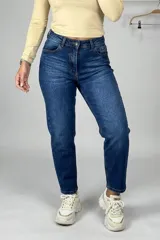 Jean estilo mom de tiro alto, confeccionado en denim azul con lavado clásico. Presenta corte recto y holgado, con cierre y botón frontal, y bolsillos laterales y traseros.