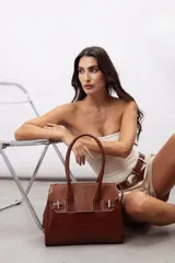 Cartera de mano estructurada de cuero vacuno rojo, con doble asa superior y detalles de charol en la parte superior. Cuenta con cierres metálicos y apliques decorativos laterales con hebillas.