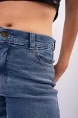 Pantalón tipo mom jean de tiro alto, confeccionado en denim rígido de color azul medio con efecto lavado. Presenta un corte recto y holgado con ruedos doblados, cierre frontal con botón y bolsillos laterales.