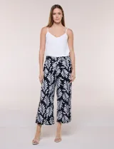 Pantalón crop de lino y rayón marca Dash, con estampado de hojas en blanco sobre fondo negro. Presenta tiro medio, pretina elástica en la parte trasera y bolsillos frontales.