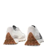Championes urbanos New Balance modelo 327, con diseño retro inspirado en los años 70. Presentan una combinación de paneles de gamuza gris claro y base de nylon blanco, con el logo 'N' sobredimensionado en cuero sintético negro en el lateral. Incluyen una entresuela de espuma blanca y una suela de goma dentada que se extiende hacia el talón.