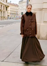 Parka de estilo encerado en color marrón, con diseño recto, cuello camisero de pana en contraste, cierre frontal con cremallera y botones, y múltiples bolsillos de parche con solapa.