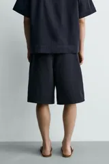 Bermuda de corte relajado confeccionada en denim de algodón rígido, con pliegues frontales, bolsillos laterales y bolsillos traseros de vivo. Cuenta con cierre frontal de cremallera y botón.
