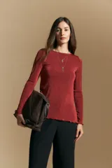 Top de manga larga con cuello redondo, confeccionado en tejido suave con un sutil acabado brillante. Presenta un corte al cuerpo, tajos laterales y terminaciones onduladas en el ruedo.