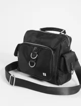 Bandolera negra de diseño versátil con múltiples bolsillos frontales y laterales, asa superior y correa larga ajustable y extraíble. Cuenta con cierre de cremallera y herrajes metálicos plateados.