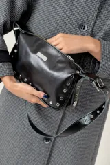 Cartera de hombro color bordó, confeccionada en cuero con acabado brillante. Presenta detalles de remaches metálicos plateados en los laterales y la base, y una correa ajustable con hebilla. Incluye una placa metálica con el logo de la marca en la parte frontal.