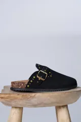 Zueco de gamuza color negro con detalle de tachas metálicas doradas en la parte superior y lateral. Cuenta con una plantilla de corcho y suela de goma antideslizante.