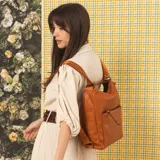 Mochila convertible en cartera de cuero sintético color suela, con bolsillo frontal con cierre, herrajes metálicos y correas regulables con inscripción de la marca.