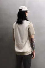 Chaleco técnico de corte regular con cuello subido y cierre frontal de cremallera. Presenta un diseño ligero con panel frontal ligeramente acolchado, bolsillos laterales con cremallera oculta y un bolsillo adicional en el pecho con tirador en color naranja. Incluye acabados con cinta elástica en el bajo y detalle de logo estampado.