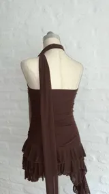 Vestido corto marrón oscuro, estilo strapless, con detalle de frunces en la cintura y falda con volados superpuestos. Incluye un accesorio tipo choker o corbatín a juego.