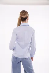 Camisa celeste con cuello clásico, abotonada al frente y decorada con apliques de perlas y strass.