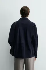 Sobrecamisa de hombre, color azul marino oscuro, confeccionada en piel con acabado ante. Presenta cuello solapa, manga larga con puños abotonados, un bolsillo de parche en el pecho y cierre frontal de botones.