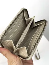 Mini billetera de cuero con textura efecto cocodrilo y cierre perimetral. Presenta un parche central con el logo de la marca grabado.
