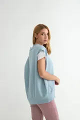 Chaleco de punto color verde, con escote en V y cierre frontal de botones negros. Presenta un diseño holgado con terminaciones acanaladas en el cuello, sisas y ruedo.