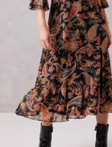 Vestido midi de gasa con estampado de arabescos en tonos cálidos sobre fondo negro. Presenta cuello alto con detalle de punto smock, mangas largas con puños elásticos y volados, y falda con tajo lateral y ruedo con volado. Incluye forro interno y cierre posterior.