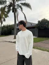 Sweater de punto con diseño bicolor y texturas combinadas, presenta un lado de tejido liso y otro con trenzado vertical. Posee cuello redondo, corte holgado y una etiqueta decorativa en el frente.